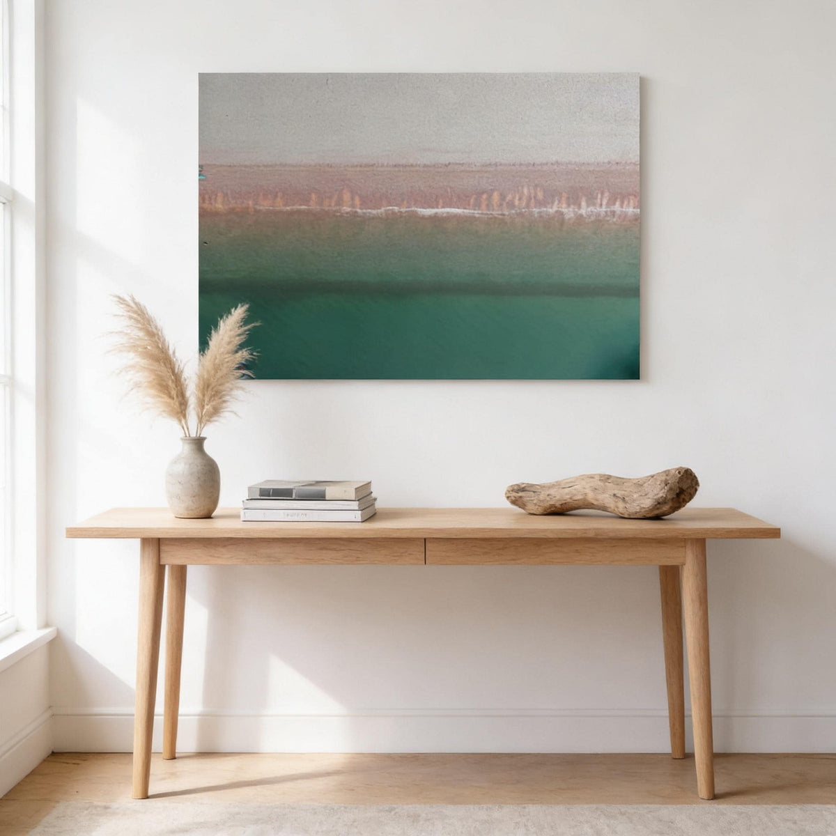 a wooden table with a stack of books and a potted plant on it, set against a white wall with a framed landscape painting hanging above.