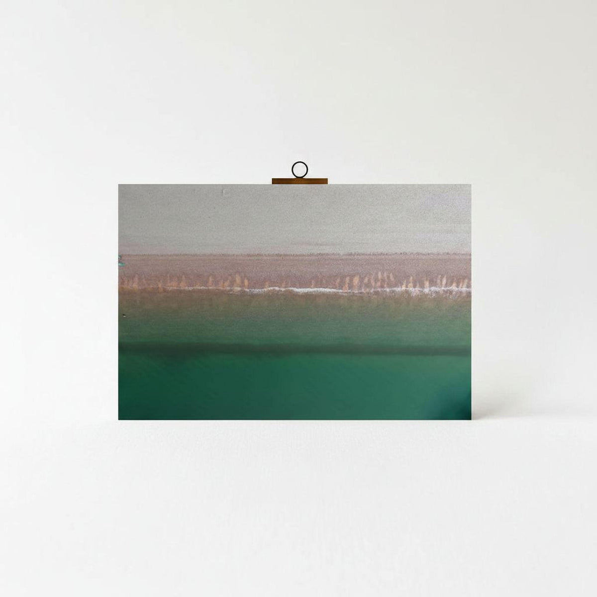 A framed photograph of a serene landscape with a greenish-blue body of water and a line of trees or vegetation in the distance.