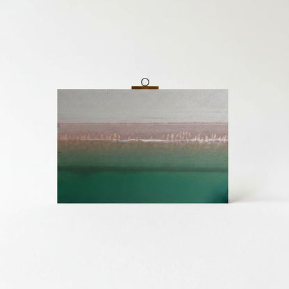 A framed photograph of a serene landscape with a greenish-blue body of water and a line of trees or vegetation in the distance.
